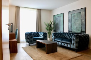 A living room with two dark blue tufted sofas, a wooden coffee table, a potted plant, and two abstract paintings on the wall.