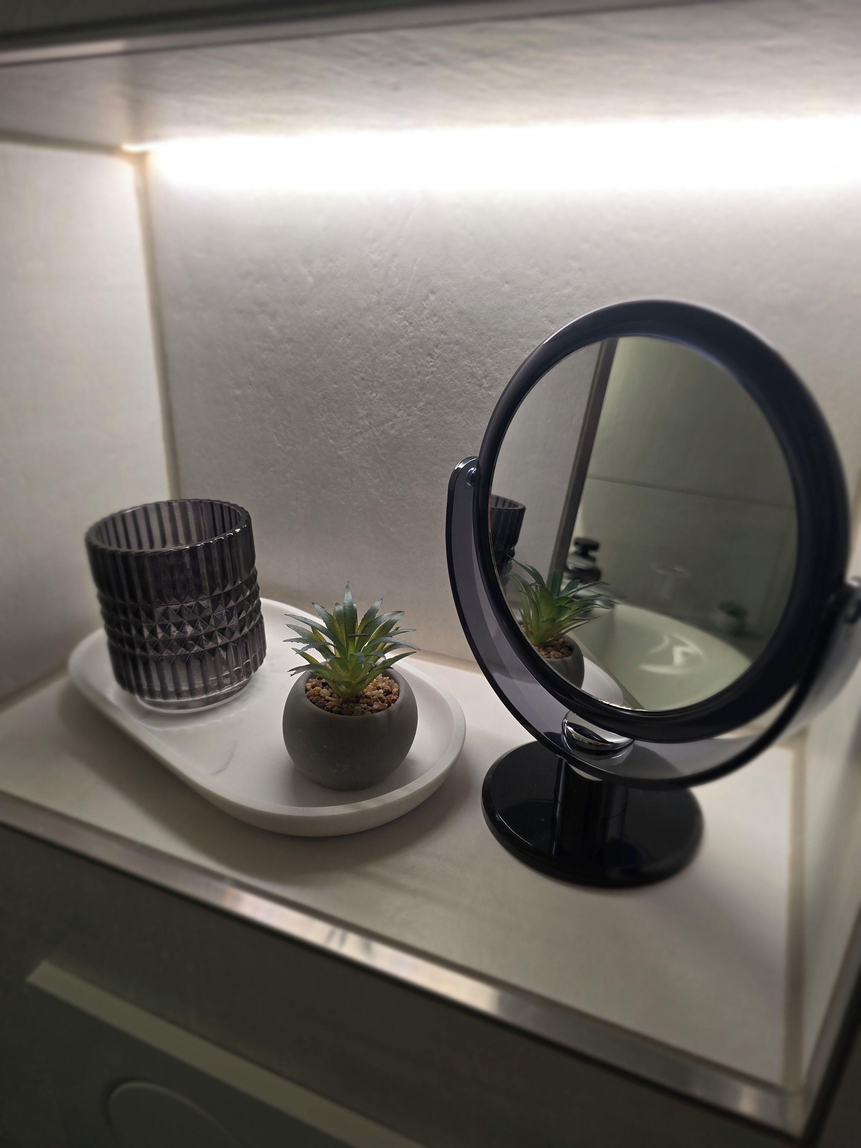A bathroom vanity with a round mirror, a textured container, and a small potted plant.