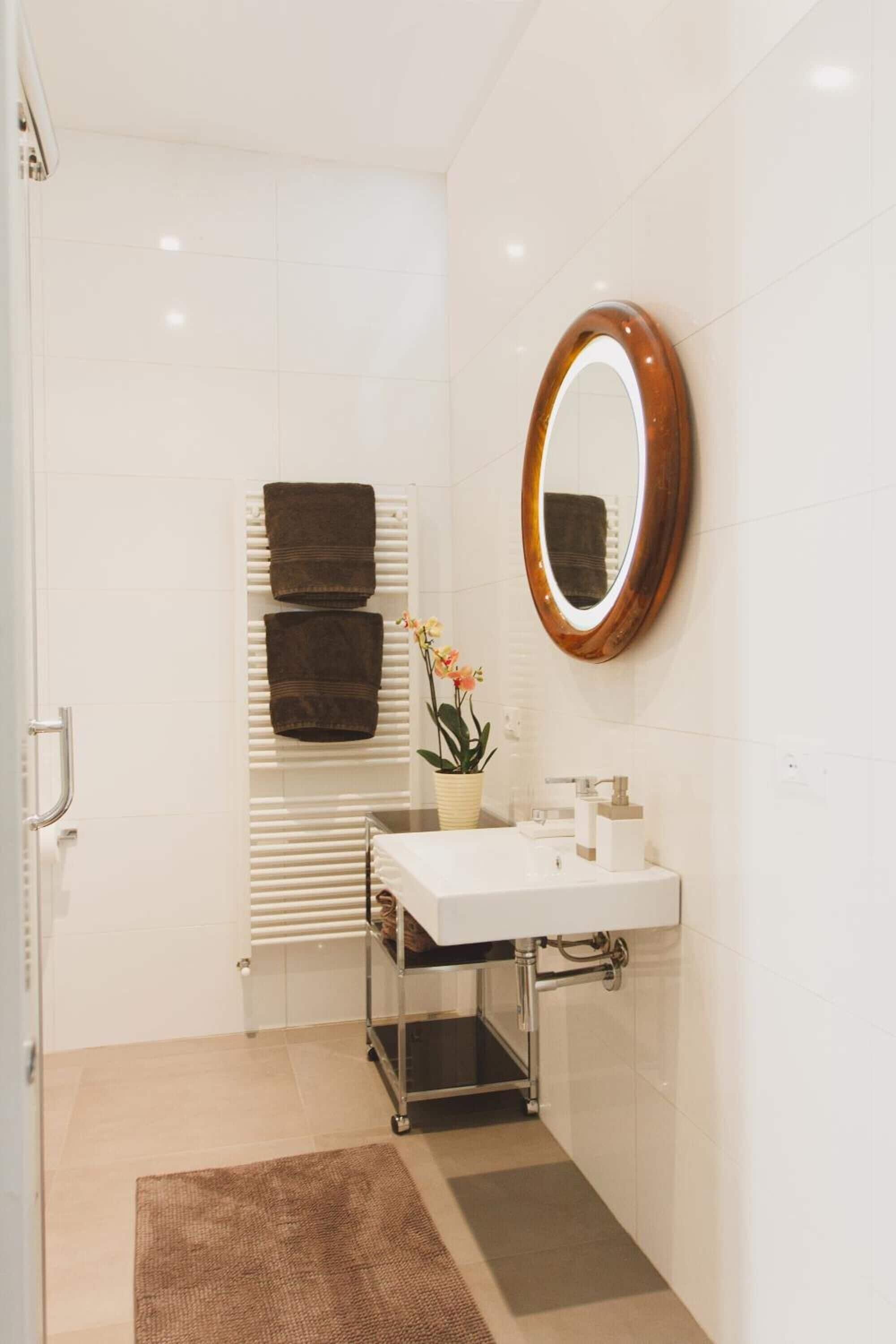 Un baño moderno con un lavamanos blanco, un espejo y dos toallas sobre una repisa.