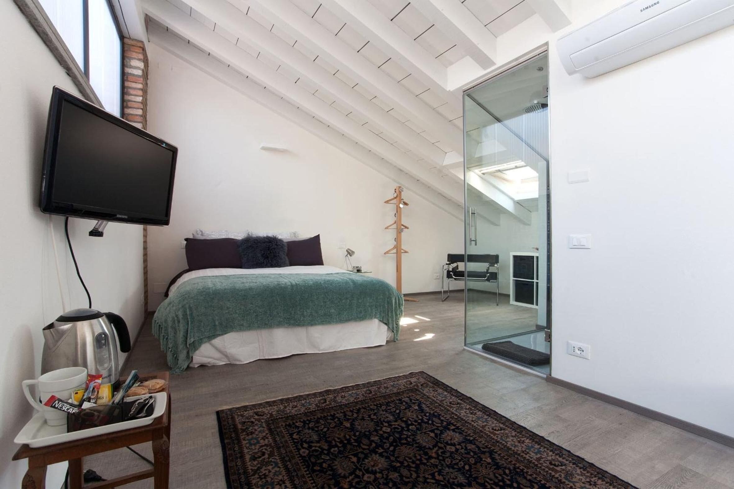 A modern bedroom with a bed, a flat-screen TV, a coffee maker, and a glass door leading to a bathroom.