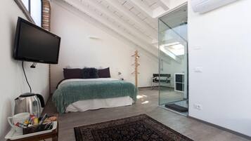A modern bedroom with a bed, a flat-screen TV, a coffee maker, and a glass door leading to a bathroom.