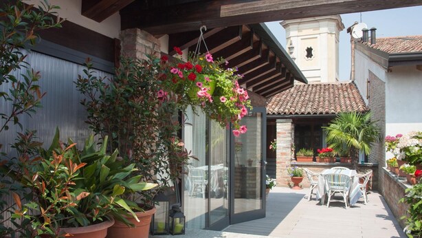 A patio with potted plants, a glass door, and a table with chairs. - B&B San Clemente (Crema)