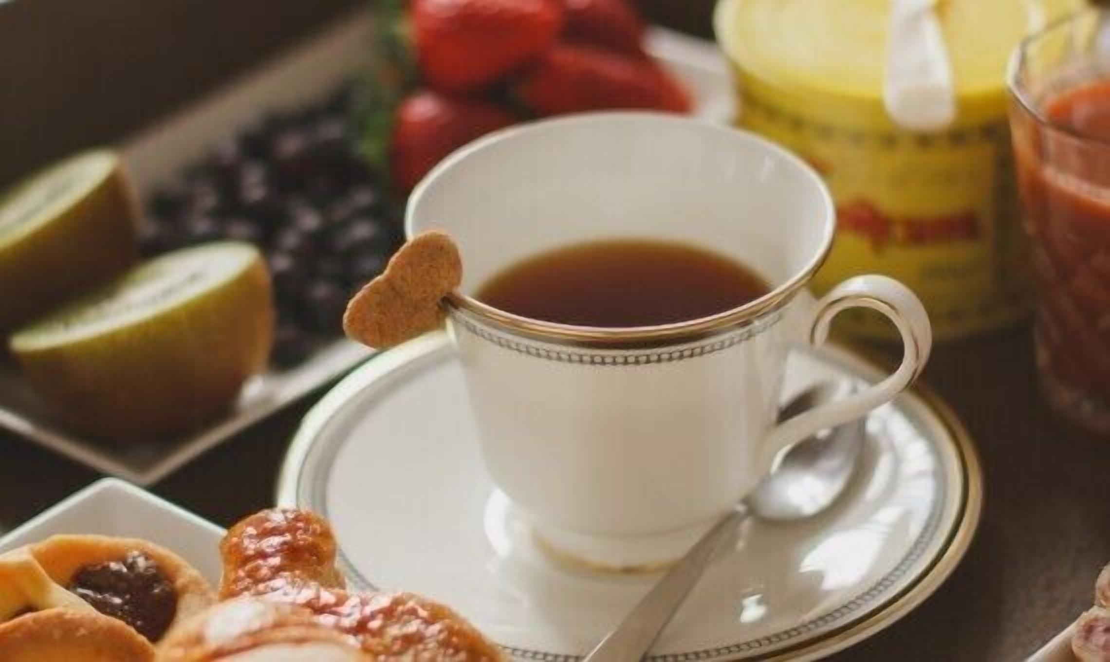A cup of tea with a biscuit on the rim, a plate with pastries, and a jar of jam.