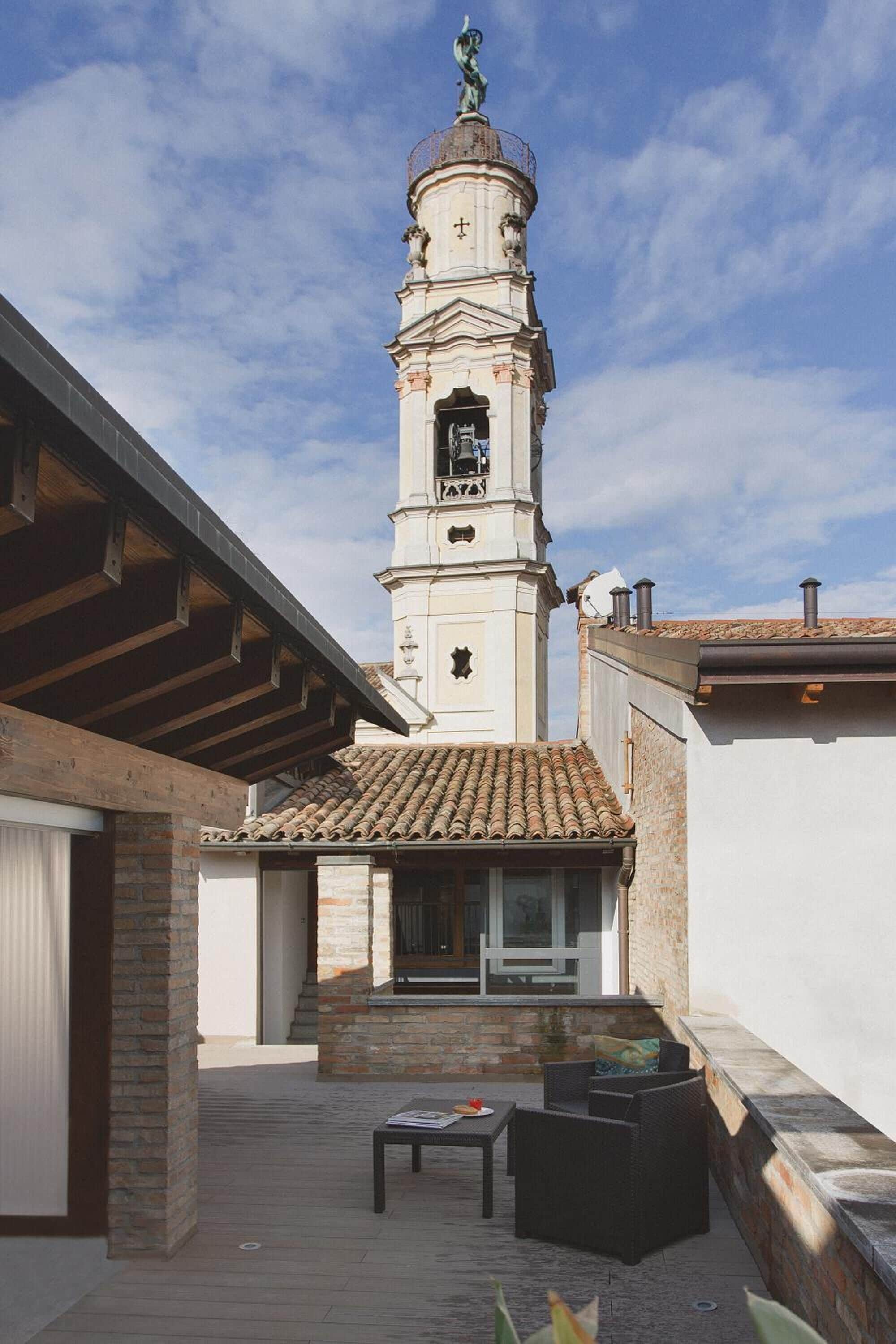 A courtyard with a tall tower, a covered patio area with a table and chairs, and a brick wall.