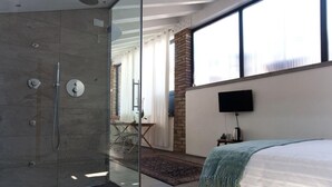 A modern bedroom with a glass shower enclosure, a large bed, a flat-screen TV, and a view of the outdoors. - B&B San Clemente (Crema)