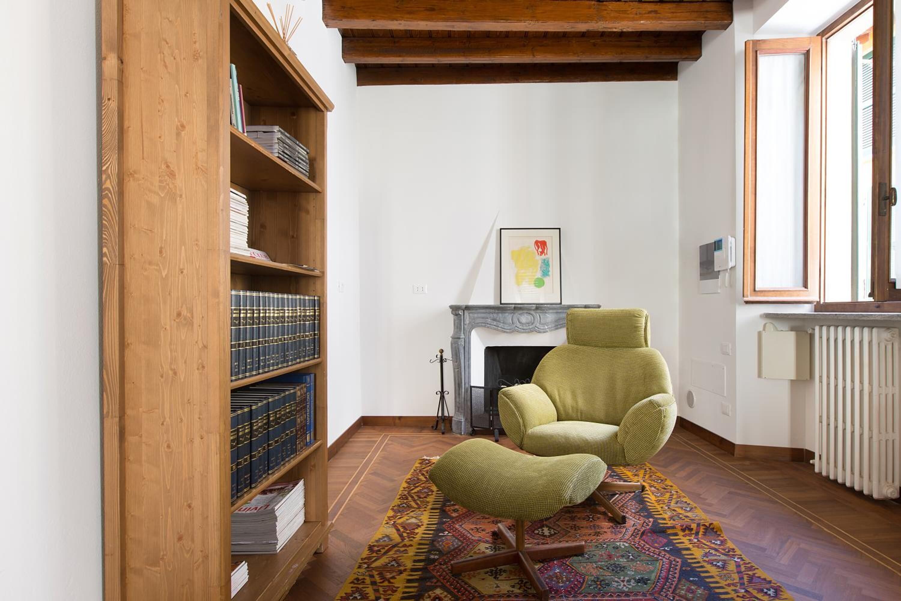 Una habitación acogedora con una estantería de madera, un sillón verde, un tapete estampado y una chimenea.