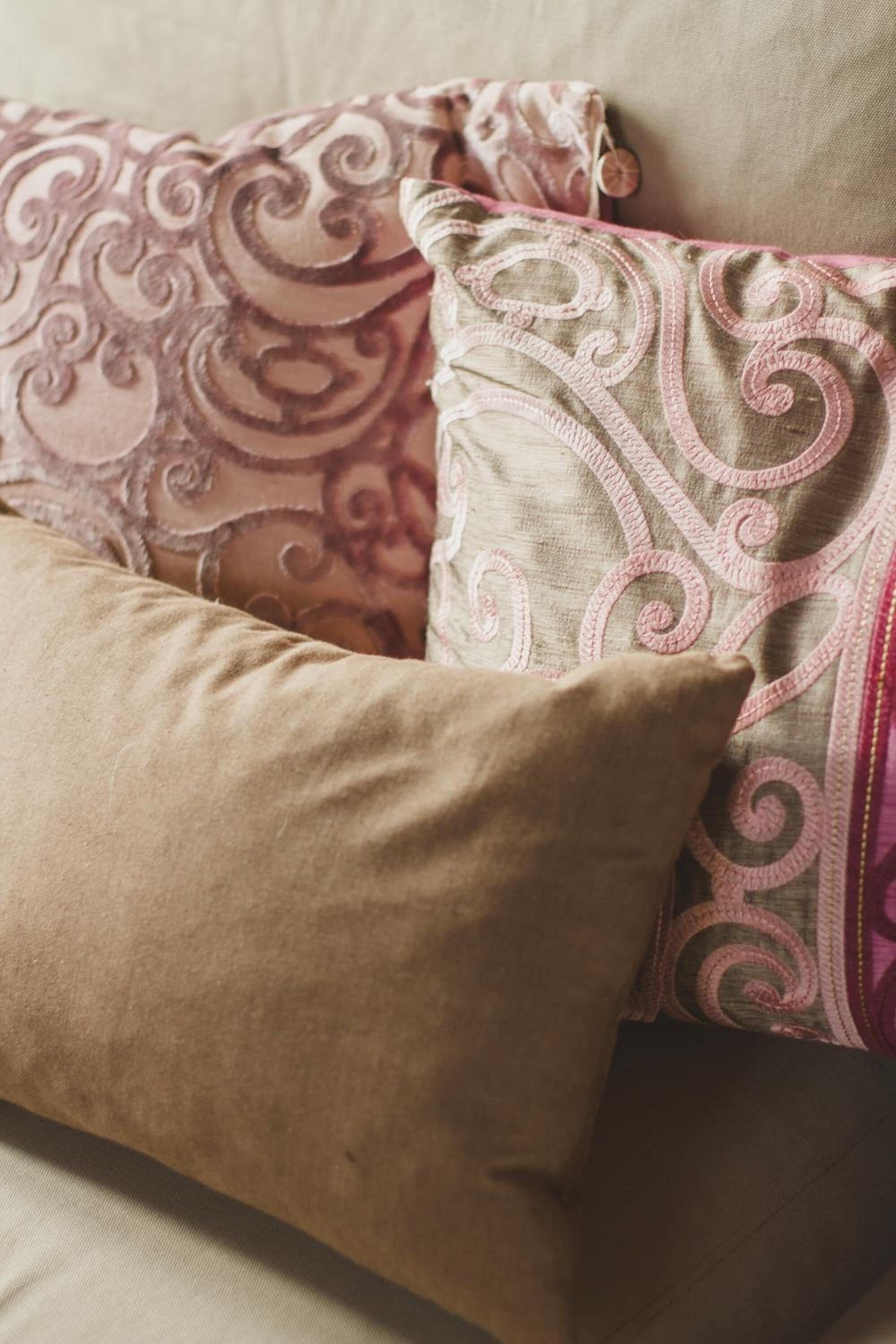 Un sofá color beige con tres almohadones decorativos.