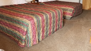 A hotel room with two beds, a wooden headboard, white pillows, a patterned bedspread, a nightstand with a lamp, and a bathroom visible through an open door. - Plaza Motel (Preston)