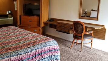 A hotel room with a bed, a desk, a chair, a television, and a mirror.