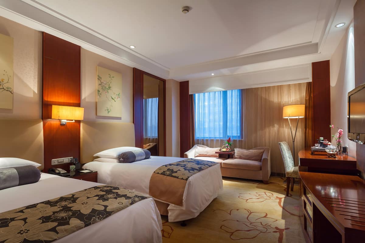 Ein Hotelzimmer mit zwei Betten, einem Sofa, einem Schreibtisch und einem Fernseher.