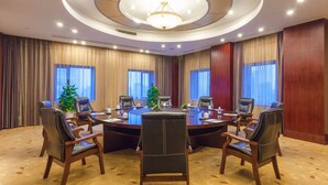 Ein Konferenzraum mit einem runden Tisch, mehreren Stühlen, einer Chandelier und großen Fenstern mit Vorhängen.