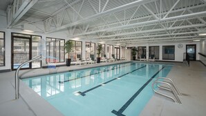 An indoor swimming pool with clear lanes, a metal ladder, and lounge chairs by the poolside.
