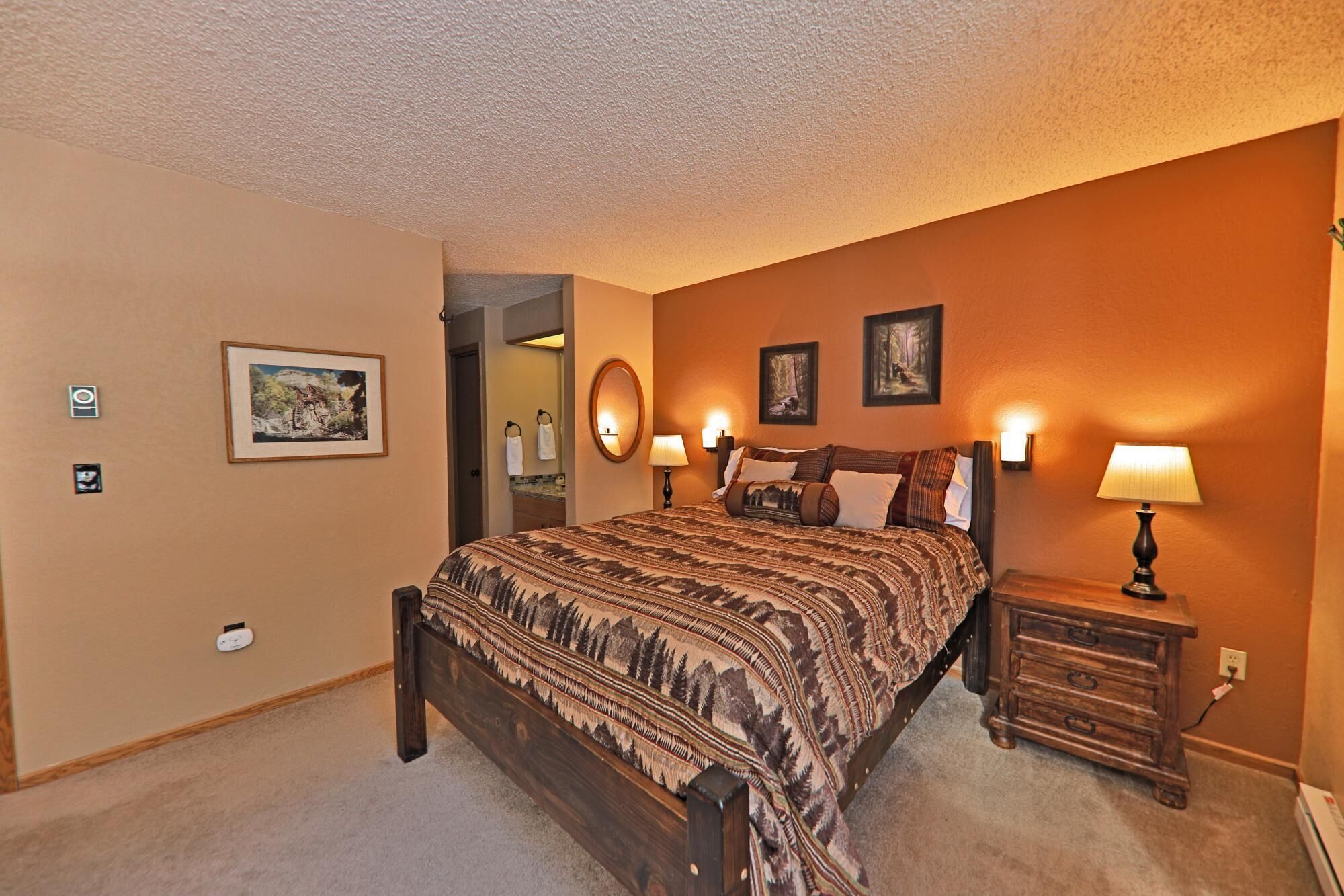 A bedroom with a large bed, a nightstand, a mirror, and two framed pictures on the wall.