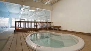 A hot tub in a spacious indoor area with wooden flooring, a wooden bench, and a view of the outside through large windows.