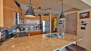 A kitchen with granite countertops, stainless steel appliances, wooden cabinets, and pendant lighting.