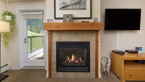 Una sala de estar con chimenea, un cuadro enmarcado encima, un televisor en la pared y una puerta que da a un balcón.