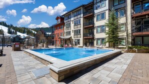 Un hotel con piscina, varios balcones y vistas a una montaña nevada.