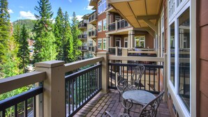 A balcony with a table and chairs, overlooking a forested area and a mountain.