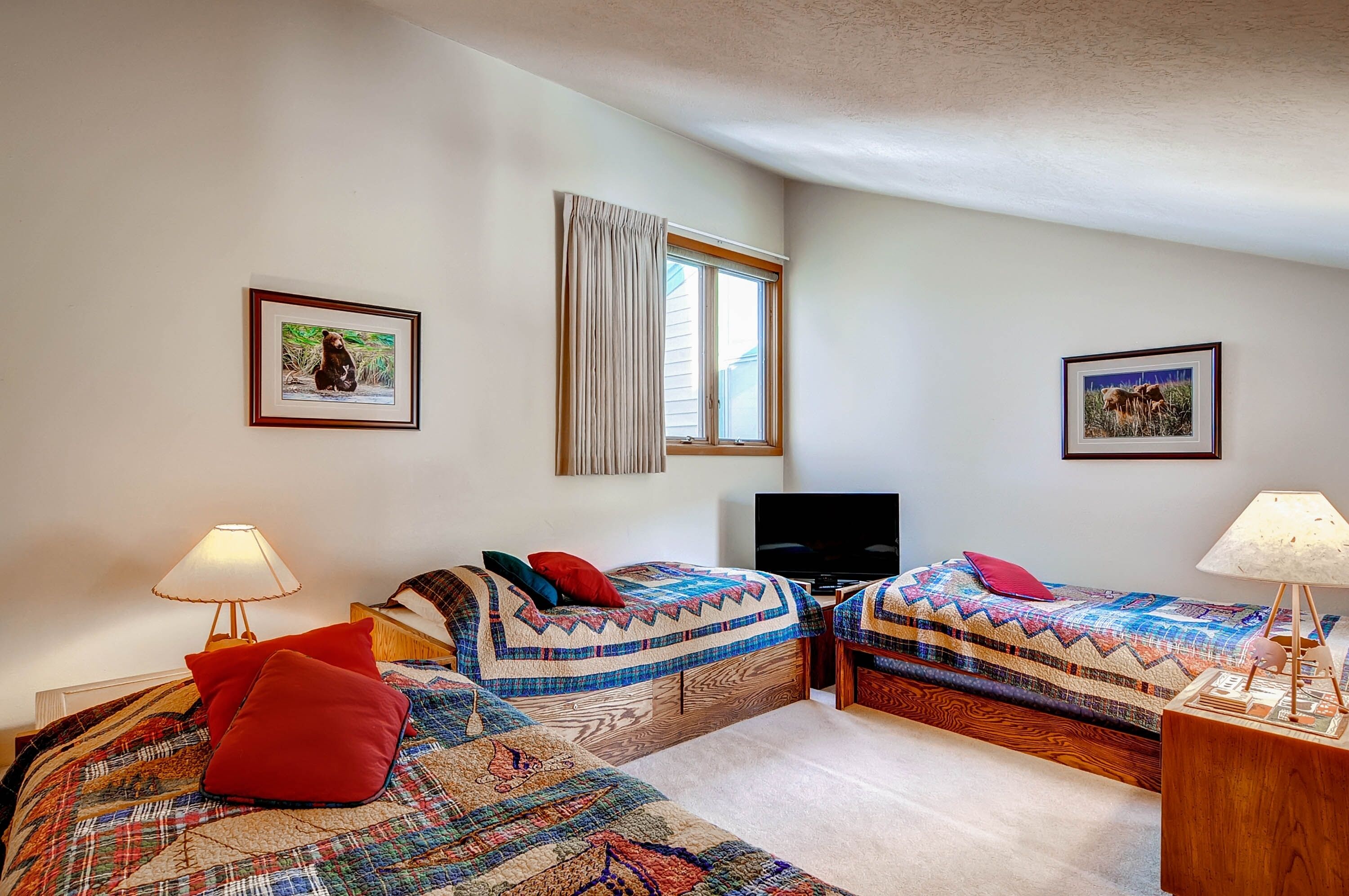 A room with two beds, a TV, and framed pictures on the walls.