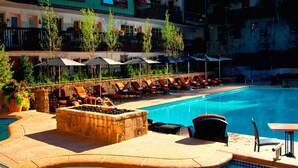 A pool area with lounge chairs and umbrellas, a stone fire pit, and a pool with a tiled edge. - Luxury Mountainside 5BR Chalet in Vail Village by RedAwning (Vail)