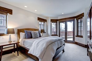Une chambre dotée d’un grand lit, de deux tables de chevet, d’une fenêtre avec des volets en bois et donnant sur le balcon extérieur.