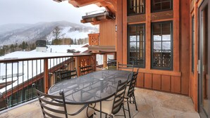 A wooden deck with a round table and chairs, overlooking a snowy landscape with mountains. - Luxury Mountainside 5BR Chalet in Vail Village by RedAwning (Vail)
