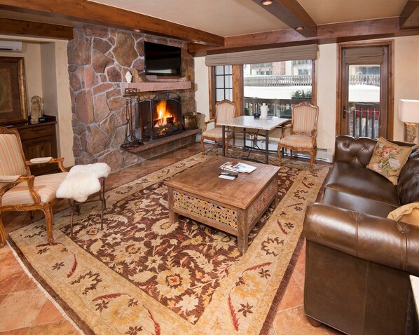 A cozy living room with a stone fireplace, leather sofa, and a television mounted on the wall.