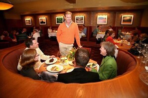 A restaurant with round tables and booths, wooden flooring, and framed pictures on the walls.