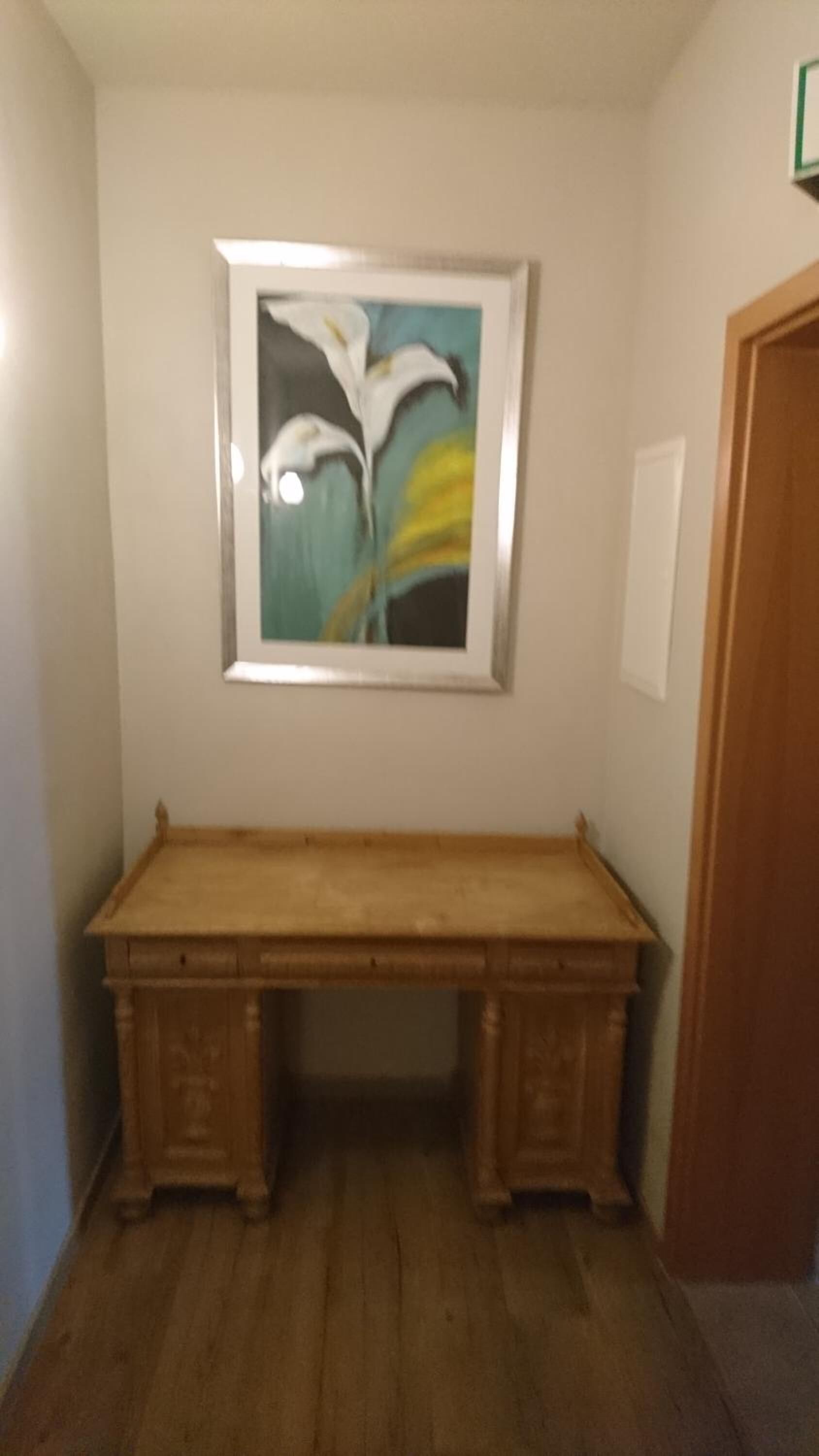A wooden desk in a room with a framed painting of flowers on the wall.