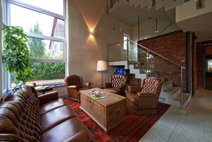 Una sala de estar moderna con muebles de cuero, una mesa de centro de madera y un ventanal con vistas a edificios y árboles.