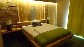 Una cama con estructura de madera, una colcha verde, dos lámparas de noche y una mesita de noche con lámpara.