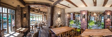 Un interior rústico con paredes de piedra, mesas de madera y lámparas colgantes.