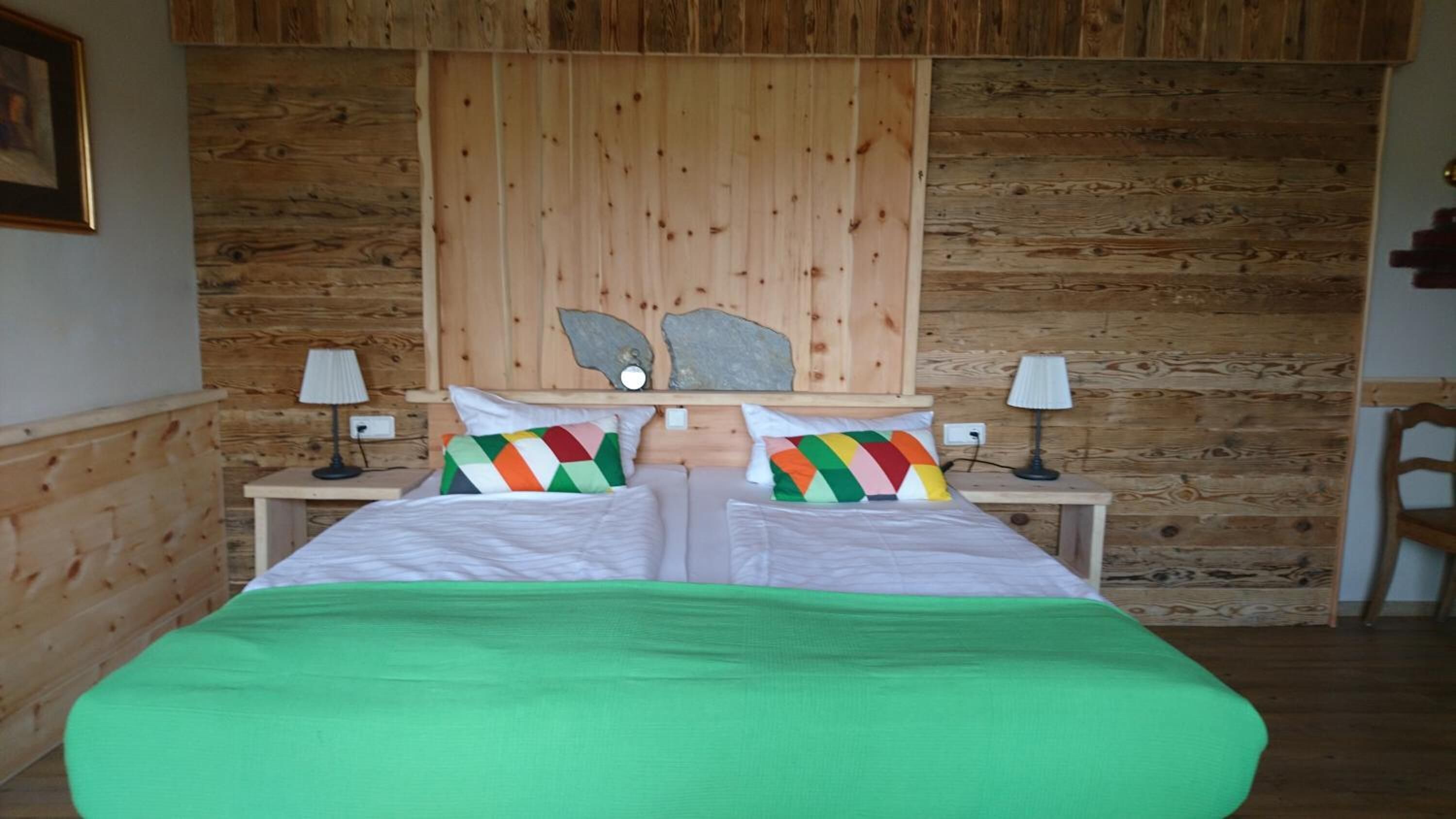 Een kamer met houten lambrisering, een bed, twee nachtkastjes en een stoel.