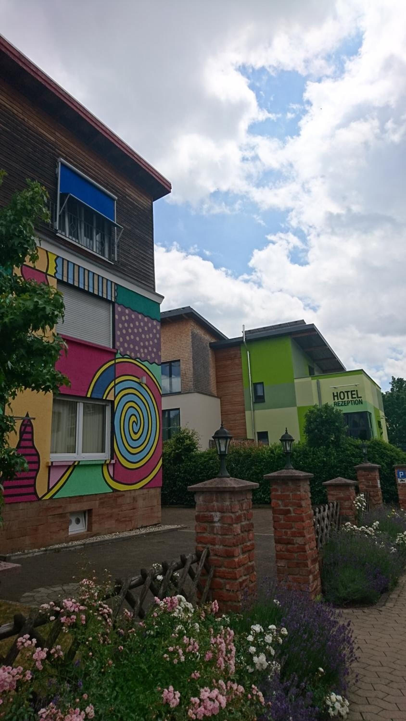 A hotel with a colorful mural on the facade, a reception area, and a landscaped garden with flowers.