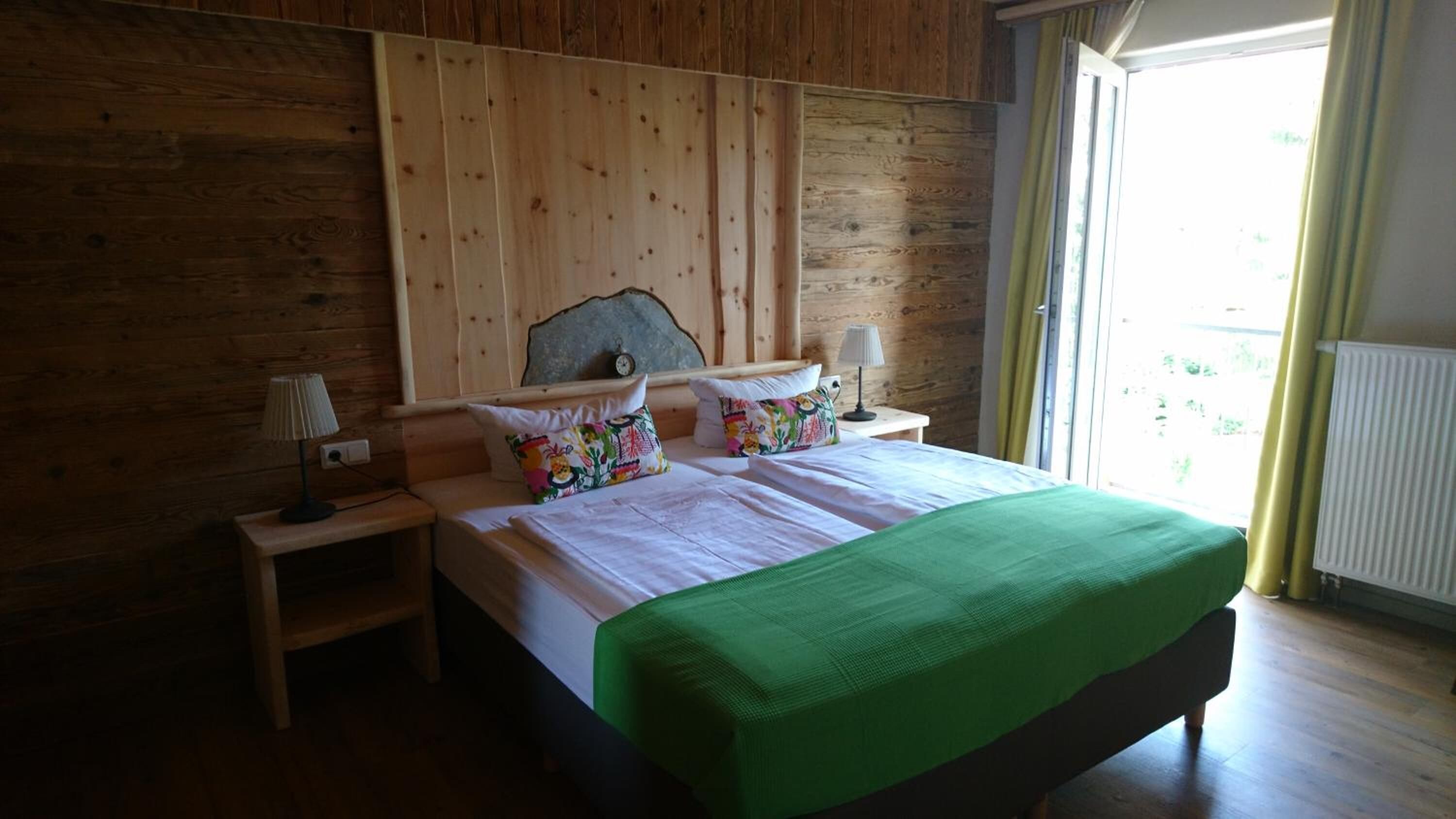 Ein Schlafzimmer mit Holzwänden, einem Bett, zwei Nachttischen und einem Fenster mit Vorhängen.