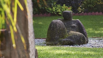 Eine Steinskulptur in einem Garten mit einer Backsteinmauer und Grünpflanzen im Hintergrund.
