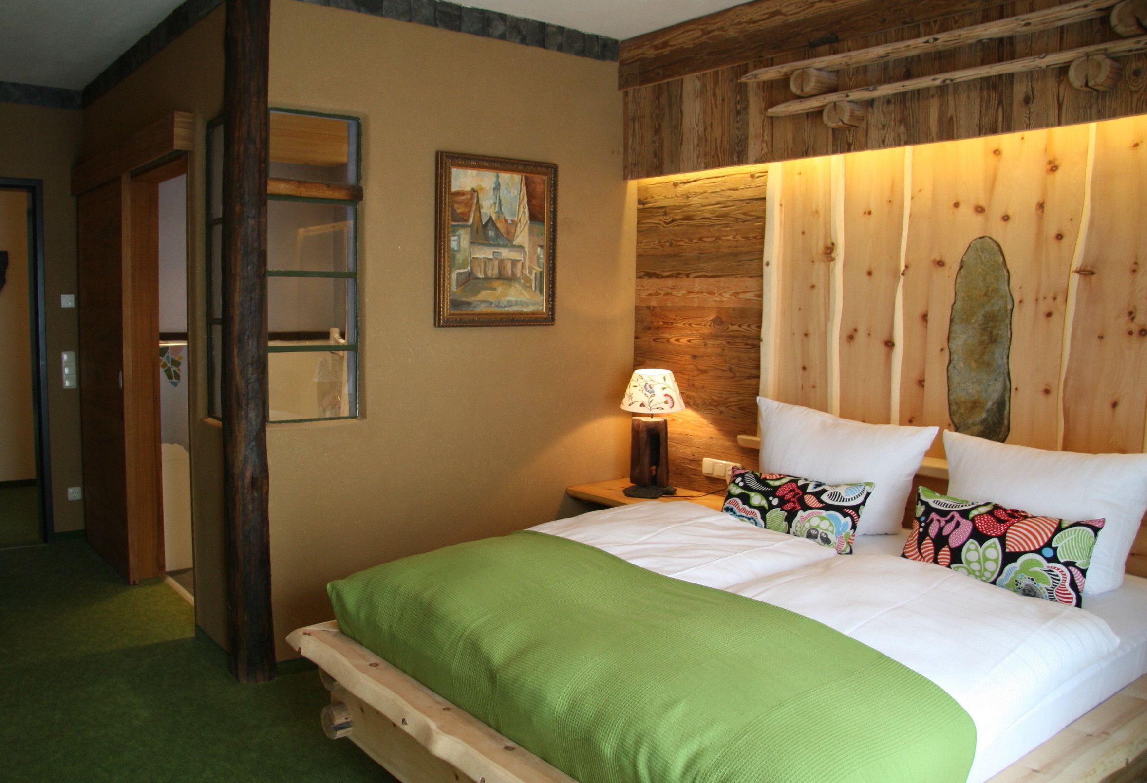 Ein Hotelzimmer mit hölzernem Kopfteil, einer grünen Bettdecke und einem Bild an der Wand.