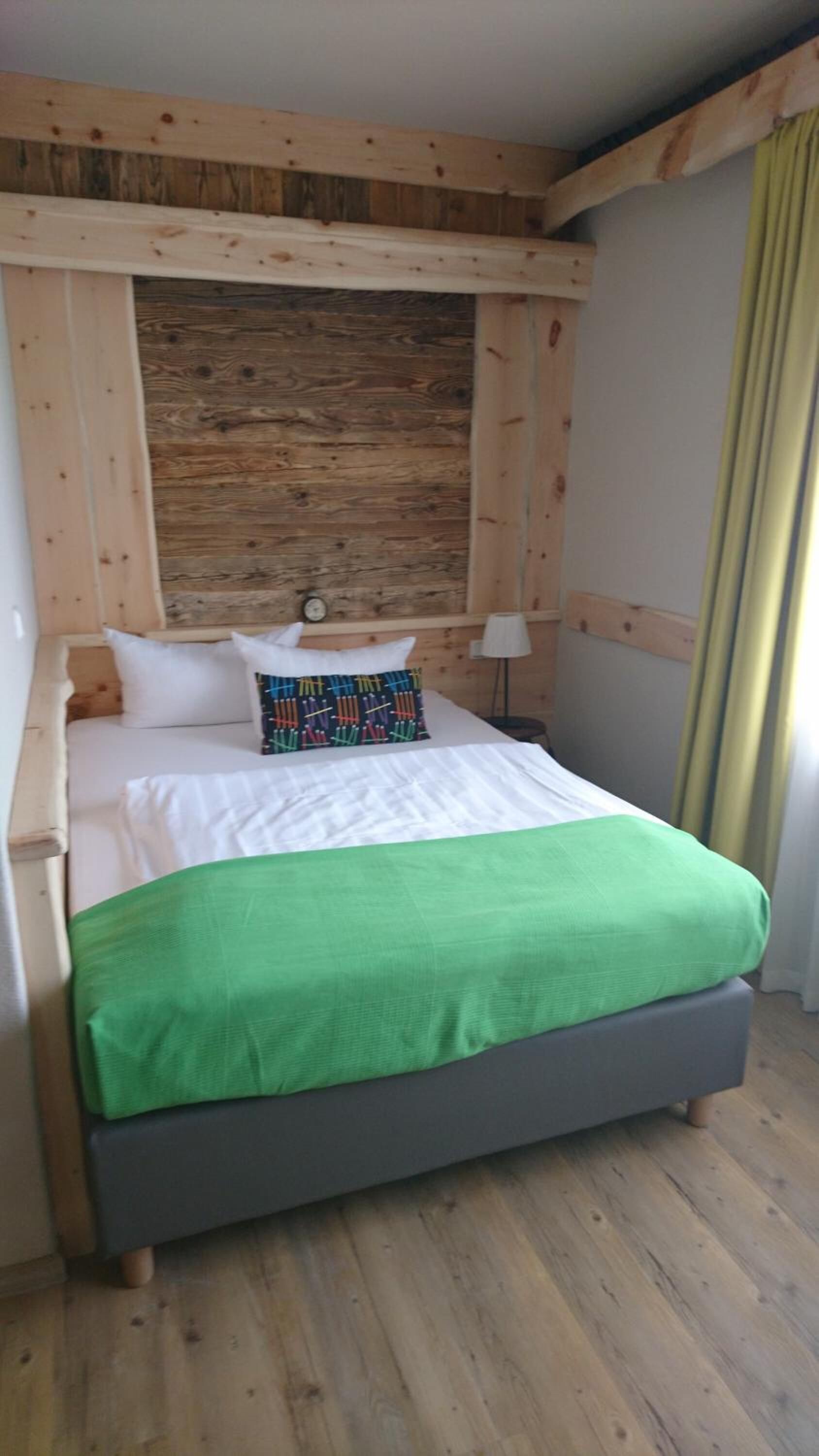 Une chambre à coucher avec un cadre en bois, un lit, des oreillers et une couverture verte.