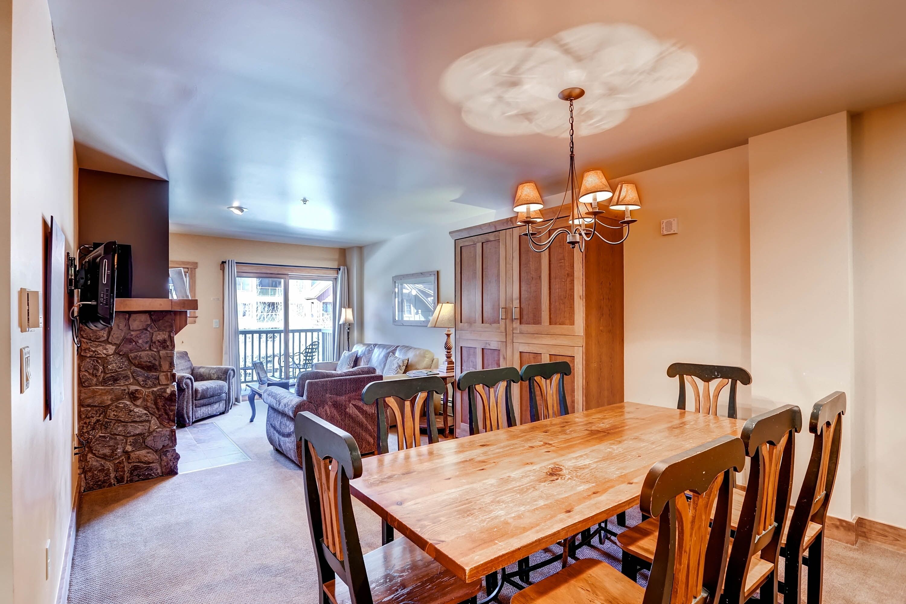 A spacious dining area with a wooden table and chairs, a stone fireplace, and a view of the living room.