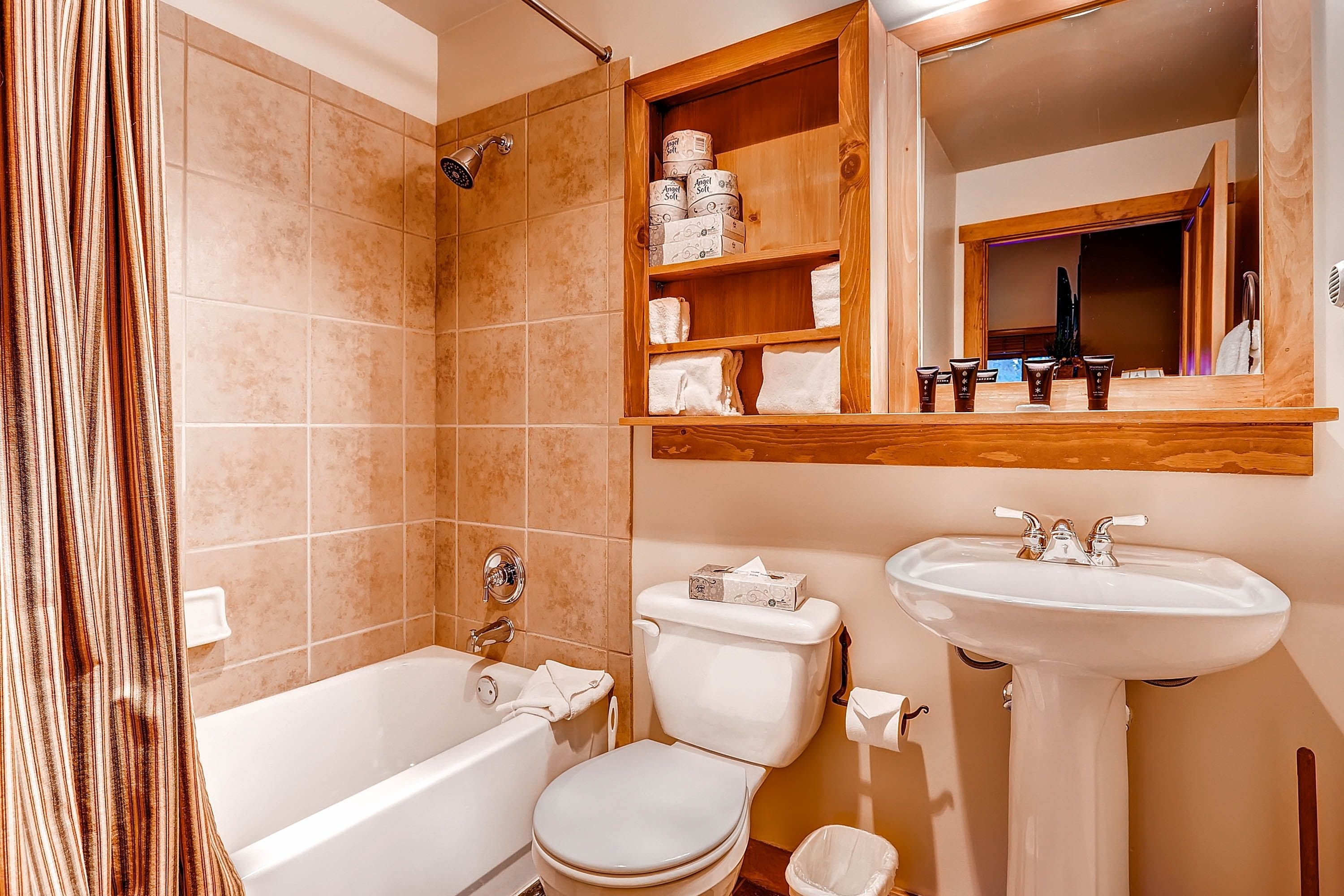 Un baño con bañera, inodoro, lavabo y estantes con artículos de aseo.