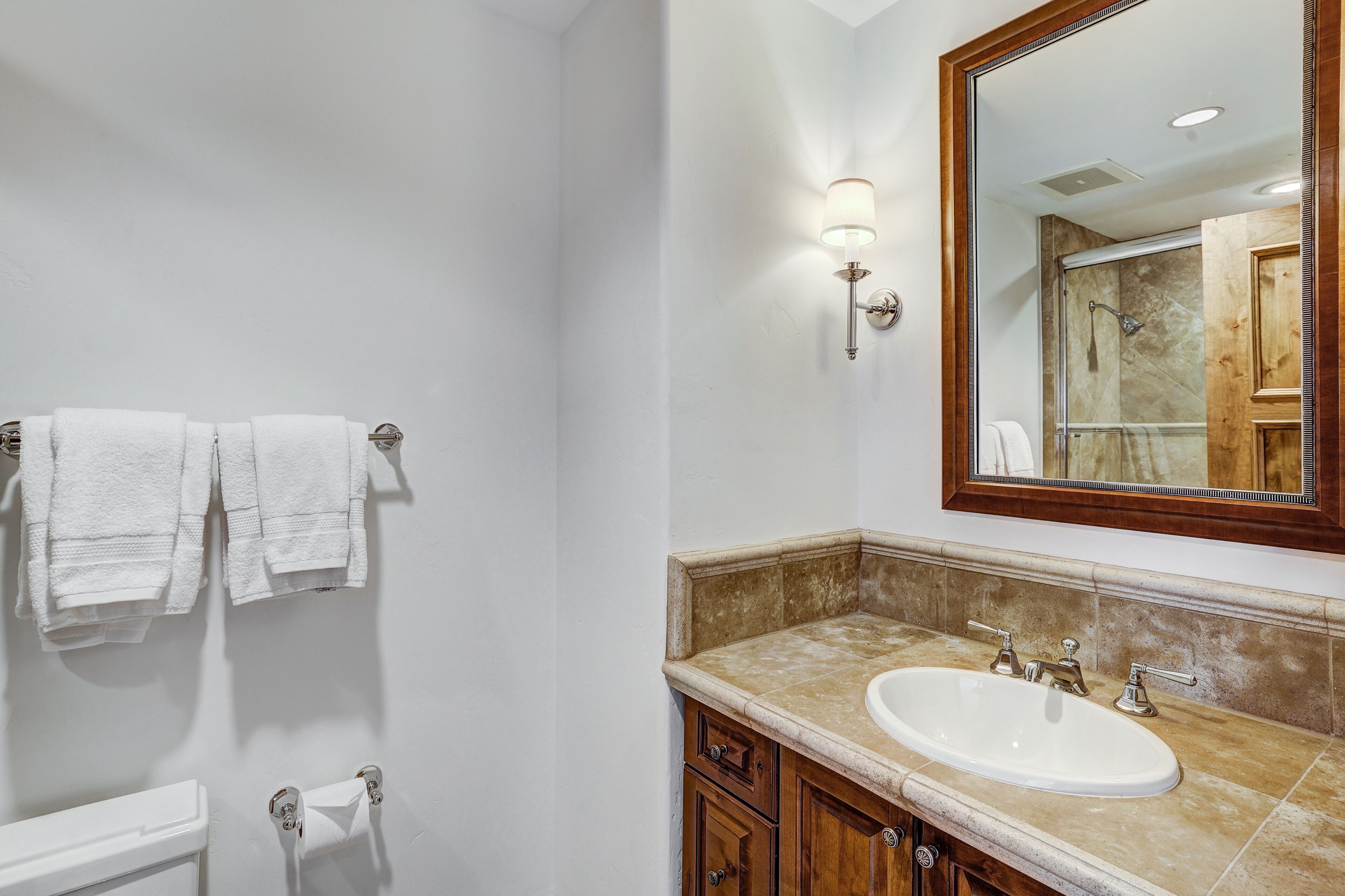 A bathroom with a white toilet, a sink with a marble countertop, and a large mirror.