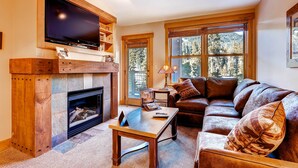 A cozy living room with a fireplace, a large flat-screen TV mounted above it, a leather sofa, and a coffee table. - Springs 8831 (Keystone)