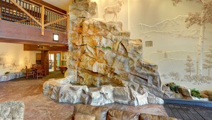 A spacious indoor area with a large rock formation centerpiece, a wooden staircase, and a mural of a mountain landscape. - Springs 8831 (Keystone)