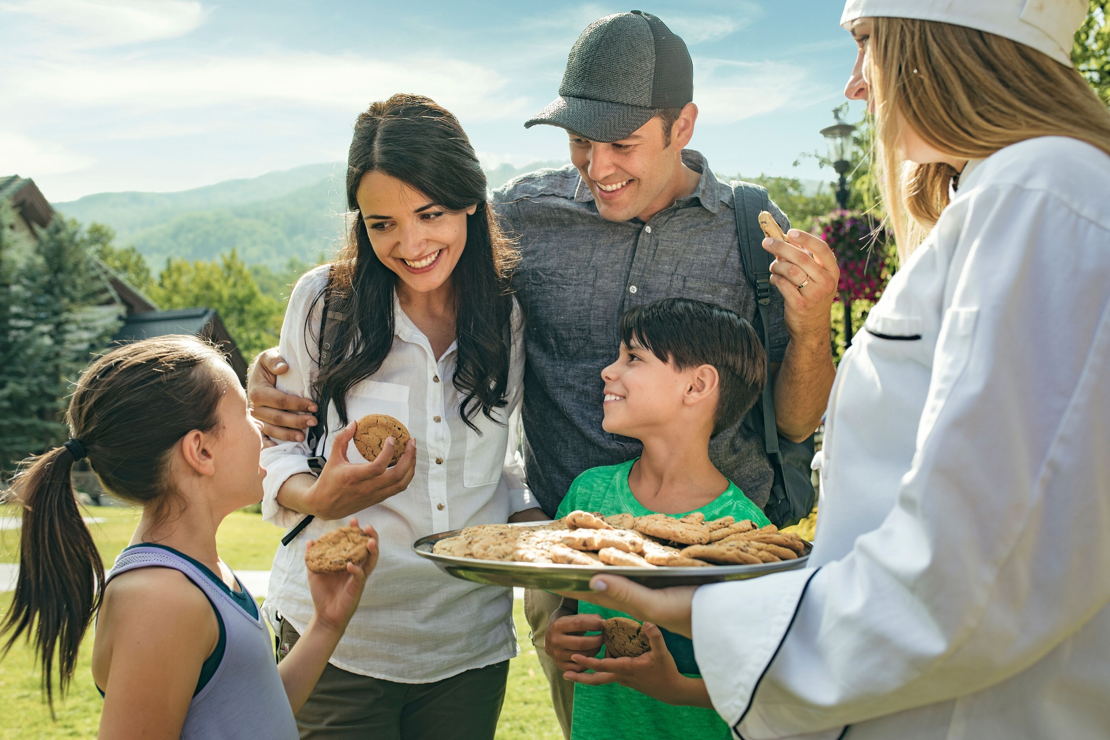 Un grupo de personas al aire libre, algunas sosteniendo galletas, con un paisaje montañoso de fondo.