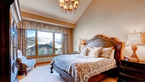 Une chambre à coucher avec un grand lit, une table de chevet, une commode, une chaise et une vue sur les montagnes par la fenêtre.