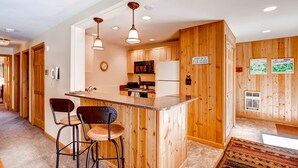 A kitchen with wooden cabinets, a central island with bar stools, and pendant lighting. - Perfect Mountain Retreat/3br -fireplace, Kids Ski Free 3 Bedroom Condo by RedAwning (Keystone)