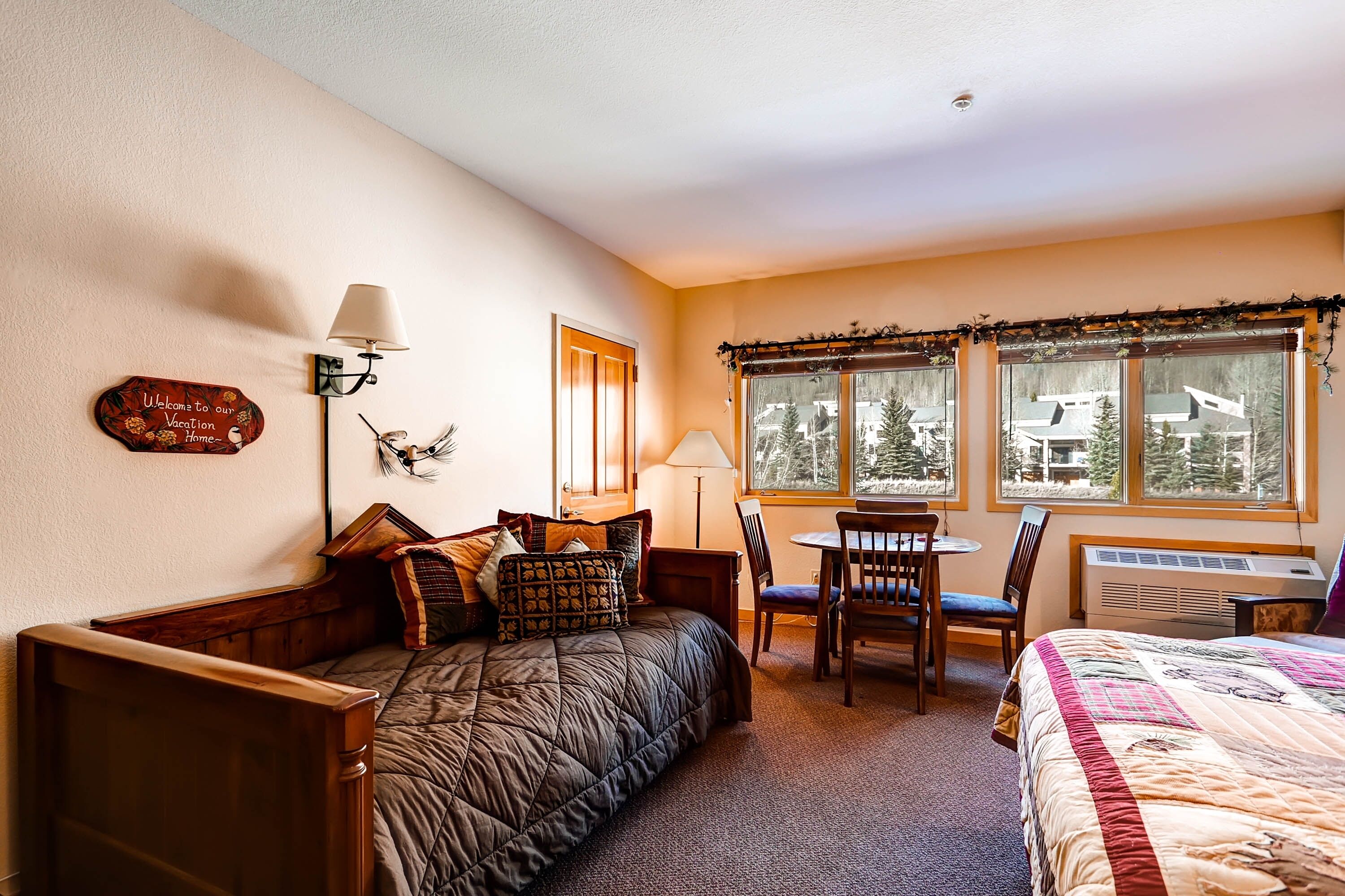 A cozy room with a bed, a desk, and a chair. There is a window with a view of trees and a building.