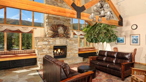 A cozy living room with a stone fireplace, wooden beams, large windows, and comfortable seating. - Gateway 5070 (Keystone)
