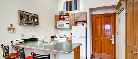 A compact kitchen with a central island, wooden cabinets, a microwave, a refrigerator, and a small dining area with two chairs.