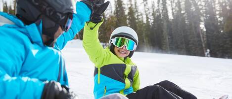 Escena nevada al aire libre con gente usando equipo de invierno, incluyendo cascos y gafas.